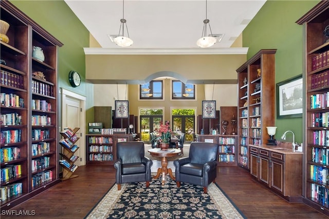 living area with ornamental molding, dark wood finished floors, and wall of books