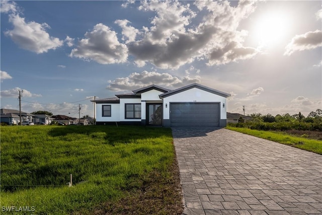single story home with decorative driveway, a garage, a front yard, and stucco siding