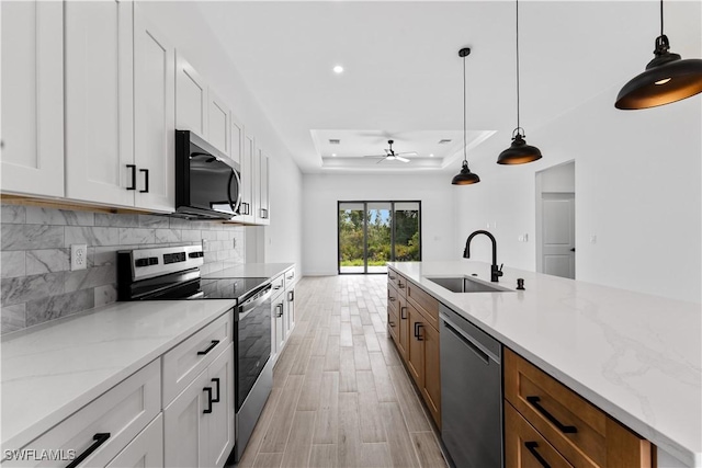 kitchen with a sink, stainless steel appliances, a ceiling fan, decorative backsplash, and a tray ceiling