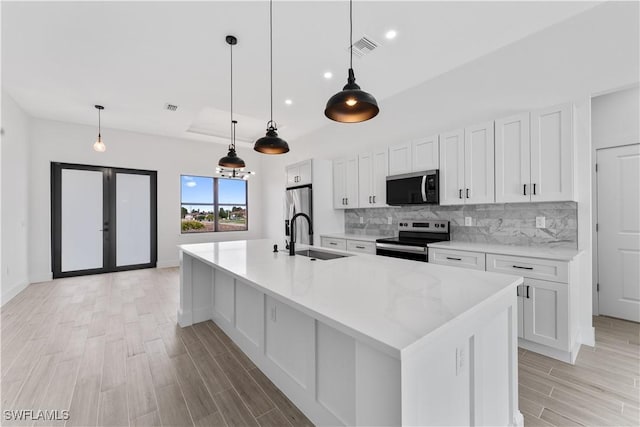 kitchen with decorative backsplash, white cabinets, a sink, light wood-style flooring, and appliances with stainless steel finishes