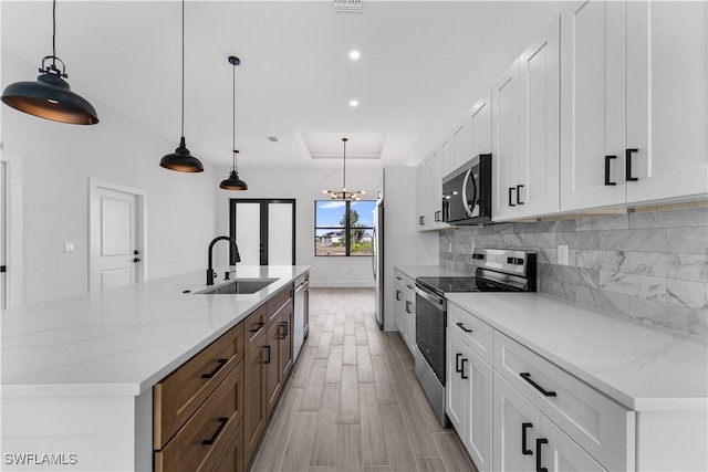 kitchen featuring a sink, a raised ceiling, stainless steel appliances, decorative backsplash, and a spacious island