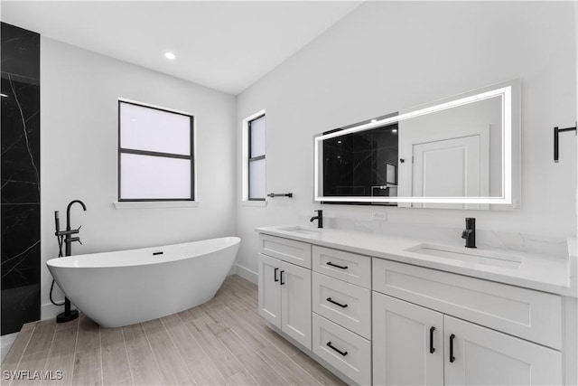 full bathroom with double vanity, a freestanding bath, a sink, and recessed lighting
