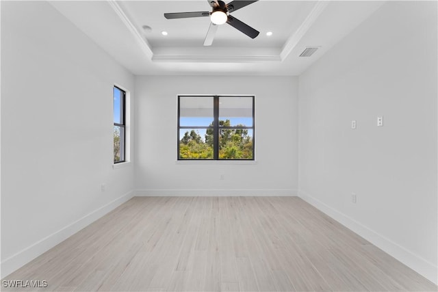 empty room with visible vents, baseboards, light wood-style floors, a raised ceiling, and a ceiling fan