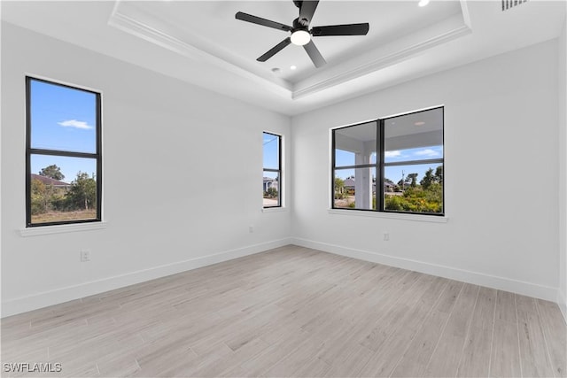 unfurnished room with baseboards, a raised ceiling, light wood finished floors, and a wealth of natural light