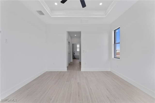 unfurnished room with ceiling fan, visible vents, light wood-type flooring, baseboards, and a tray ceiling