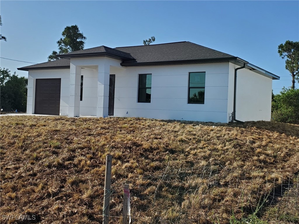 view of front of house with a garage, roof with shingles, and stucco siding