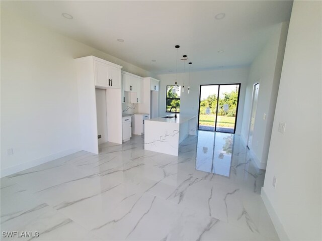 3117 35th St SW, Lehigh Acres, FL 33976 - kitchen featuring baseboards, white cabinetry, a sink, a center island with sink, and pendant lighting