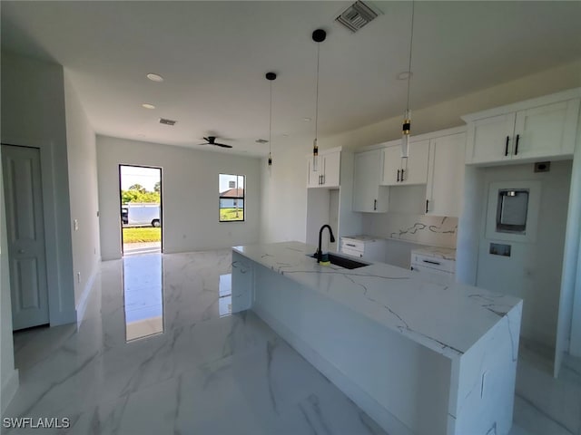3117 35th St SW, Lehigh Acres, FL 33976 - kitchen featuring a sink, white cabinets, light marble finish flooring, a kitchen island with sink, and light stone counters