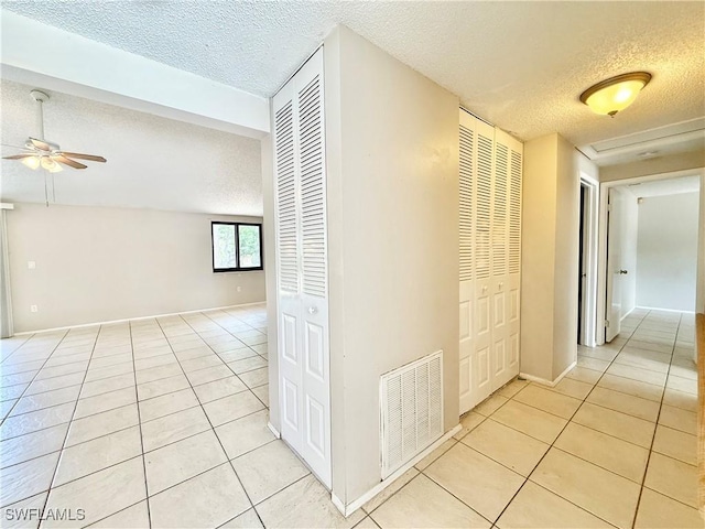hallway featuring light tile patterned floors, baseboards, a textured ceiling, and visible vents