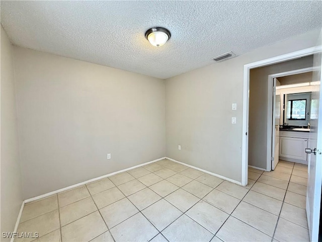 unfurnished room featuring light tile patterned floors, baseboards, a textured ceiling, and visible vents
