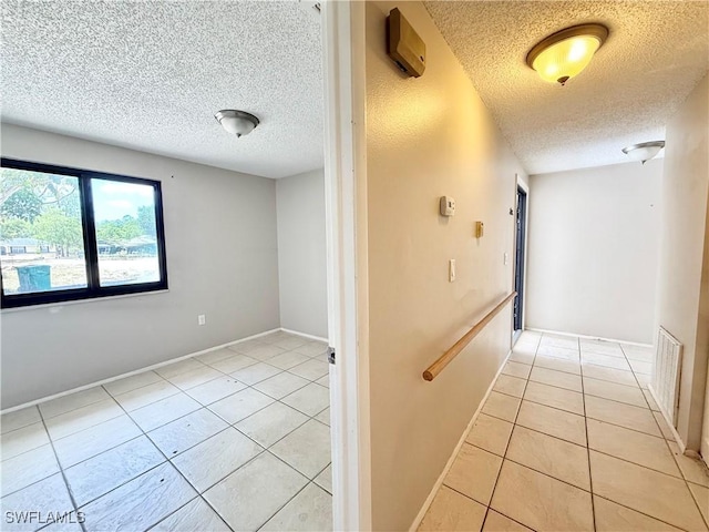 hallway with baseboards, a textured ceiling, visible vents, and light tile patterned floors