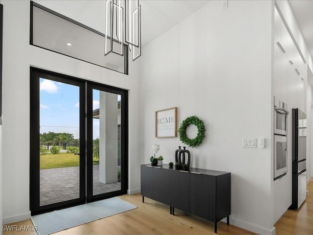 foyer featuring baseboards, a high ceiling, and light wood finished floors