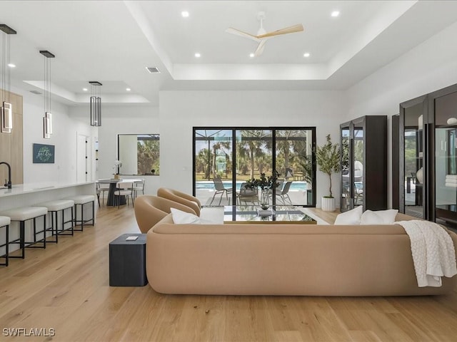 living room with a tray ceiling, visible vents, a healthy amount of sunlight, and light wood finished floors