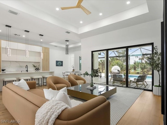 living room with recessed lighting, a raised ceiling, and light wood-style floors