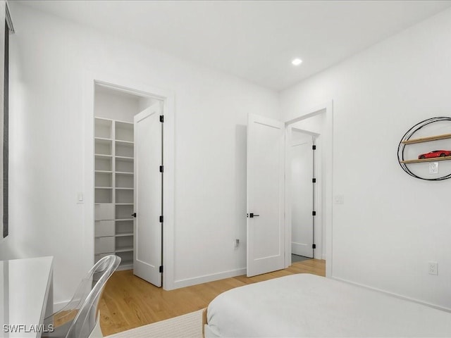 bedroom with recessed lighting, baseboards, light wood-type flooring, and a spacious closet