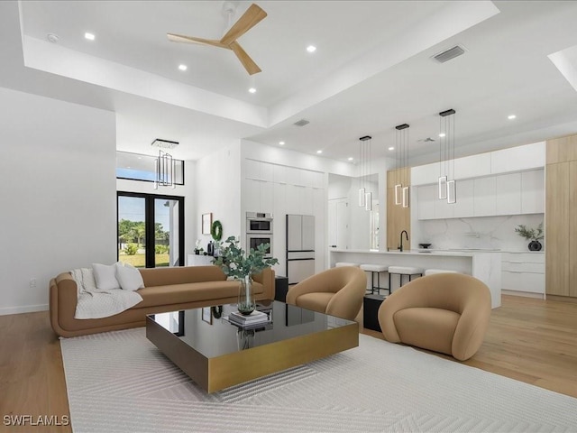 living room featuring ceiling fan, light wood finished floors, recessed lighting, a tray ceiling, and visible vents