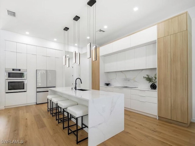 kitchen featuring visible vents, freestanding refrigerator, a breakfast bar, modern cabinets, and black electric stovetop