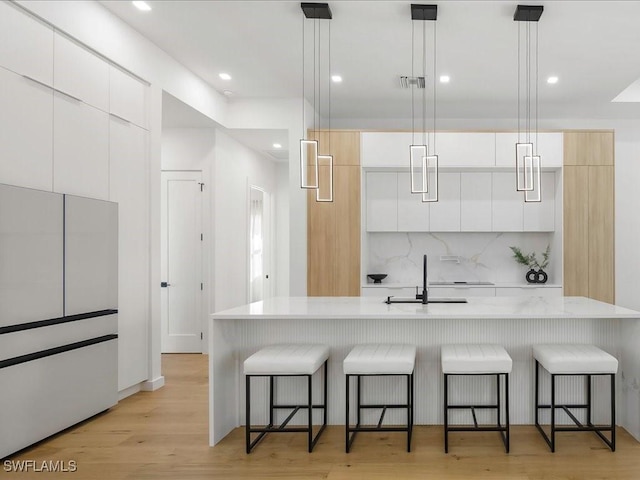 kitchen featuring a sink, decorative backsplash, modern cabinets, and a kitchen bar