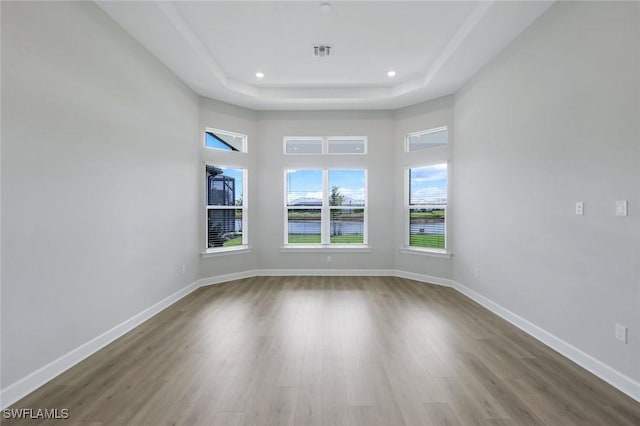 empty room with wood finished floors, visible vents, recessed lighting, a raised ceiling, and baseboards