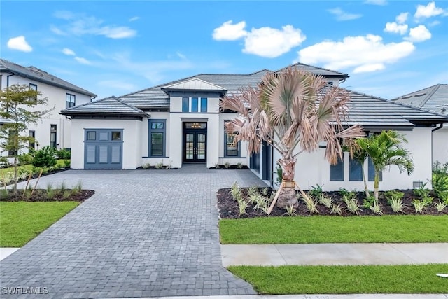 view of front of property with a front lawn, decorative driveway, stucco siding, and french doors