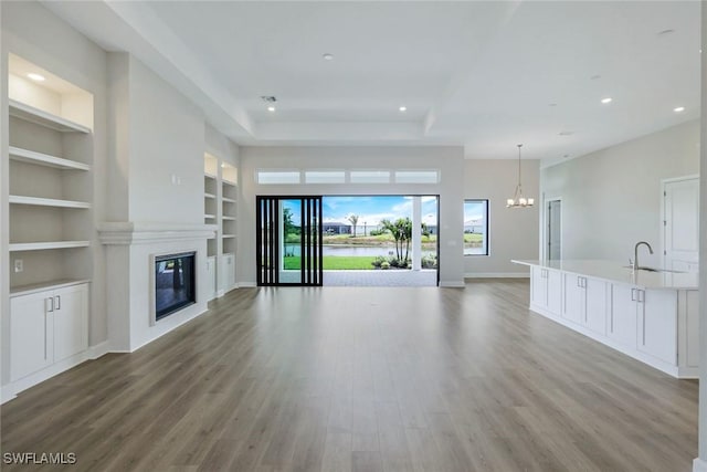 unfurnished living room with a glass covered fireplace, built in shelves, an inviting chandelier, and wood finished floors