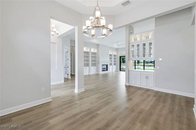 unfurnished dining area with baseboards, visible vents, a chandelier, a towering ceiling, and light wood-type flooring