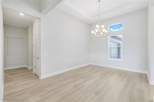 unfurnished room featuring an inviting chandelier, light wood-style floors, and baseboards