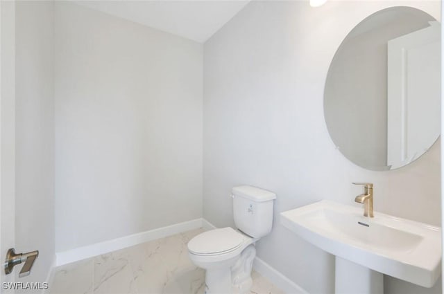 bathroom featuring a sink, toilet, baseboards, and marble finish floor