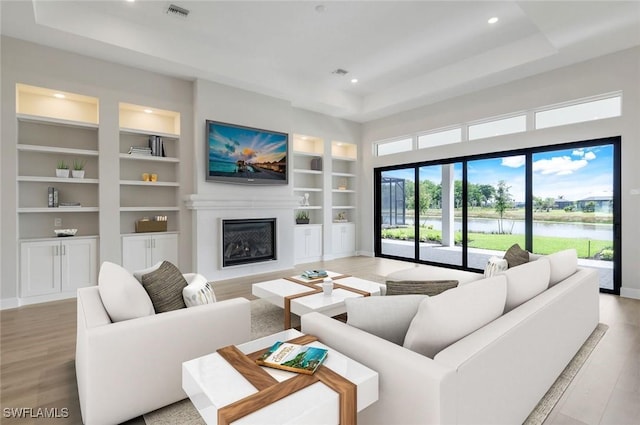 living area with a tray ceiling, light wood-style flooring, visible vents, and built in features
