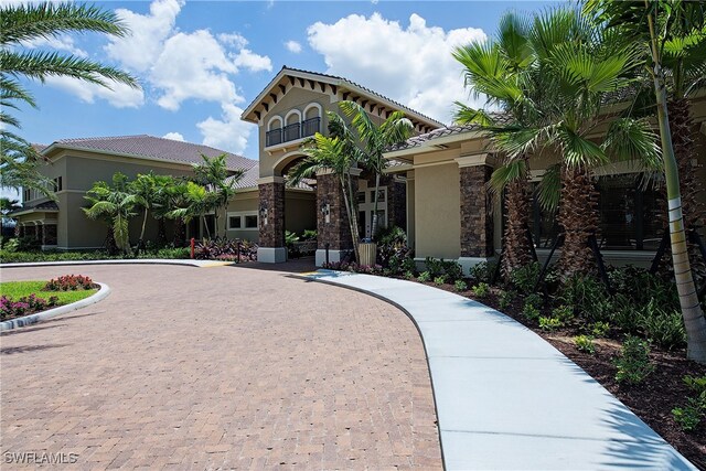 view of front of house featuring curved driveway, stucco siding, a tiled roof, and stone siding