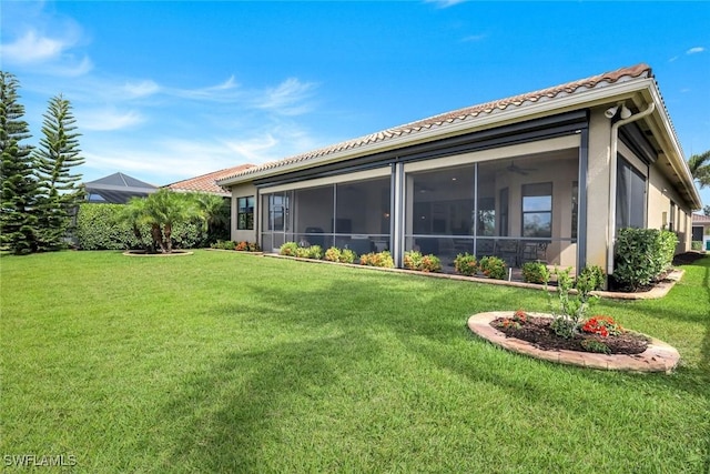 rear view of house featuring a lawn, a sunroom, a tile roof, and stucco siding