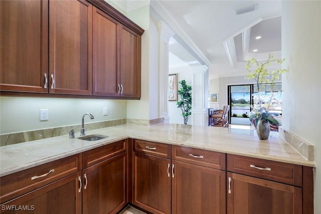 kitchen featuring a sink, light stone countertops, a peninsula, decorative columns, and ornamental molding