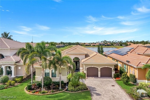 mediterranean / spanish-style home featuring a tile roof, a garage, stucco siding, decorative driveway, and a front yard