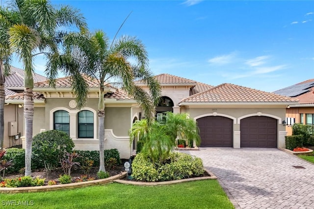 mediterranean / spanish-style home featuring stucco siding, an attached garage, decorative driveway, and a tile roof