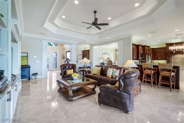 living room with ornate columns, ceiling fan, a tray ceiling, and crown molding