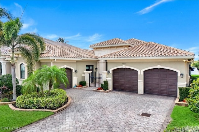mediterranean / spanish-style home featuring an attached garage, stucco siding, decorative driveway, a tile roof, and a gate