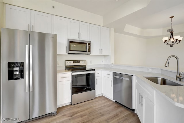 kitchen with a peninsula, white cabinetry, a sink, appliances with stainless steel finishes, and a notable chandelier