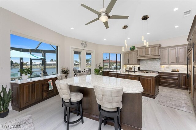 1255 Eider Ct, Punta Gorda, FL 33950 - kitchen featuring a kitchen island with sink, decorative backsplash, ceiling fan, pendant lighting, and light stone countertops
