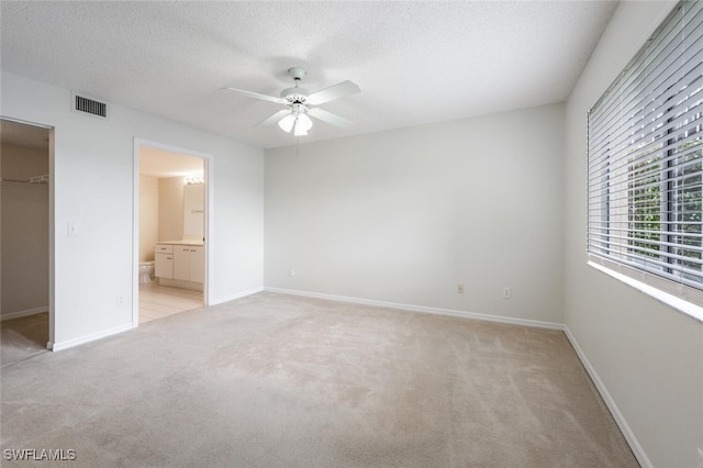 unfurnished bedroom featuring a spacious closet, light colored carpet, baseboards, a textured ceiling, and ensuite bath