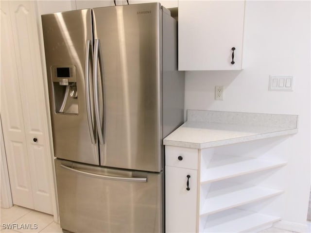 kitchen with stainless steel fridge, light countertops, white cabinets, open shelves, and light tile patterned flooring