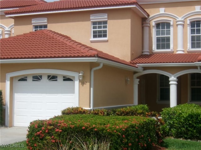 mediterranean / spanish home with a tiled roof, stucco siding, an attached garage, and concrete driveway