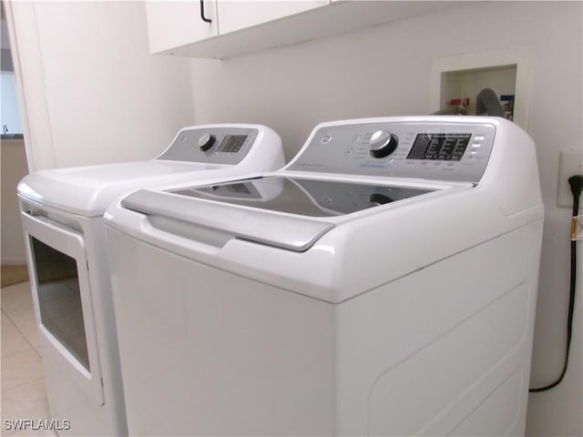 clothes washing area with washing machine and dryer, cabinet space, and light tile patterned floors