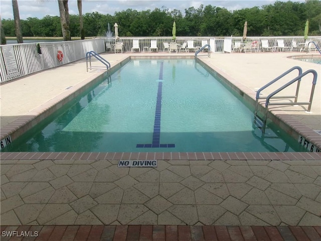 community pool with a patio area, fence, and view of wooded area