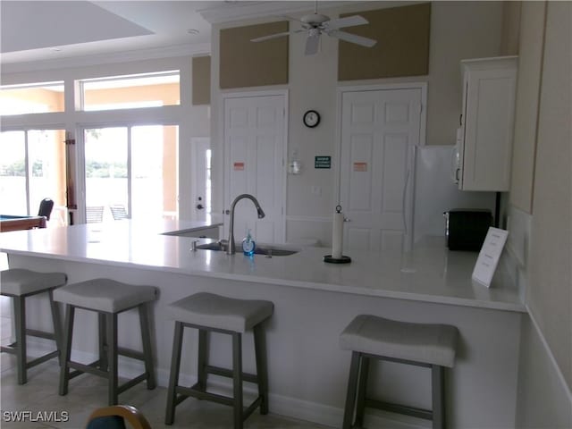 kitchen featuring a sink, a ceiling fan, a peninsula, a breakfast bar, and light countertops