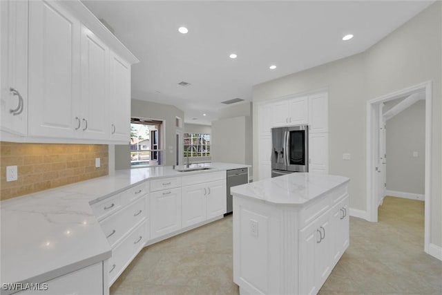 kitchen featuring a peninsula, a sink, white cabinetry, appliances with stainless steel finishes, and tasteful backsplash