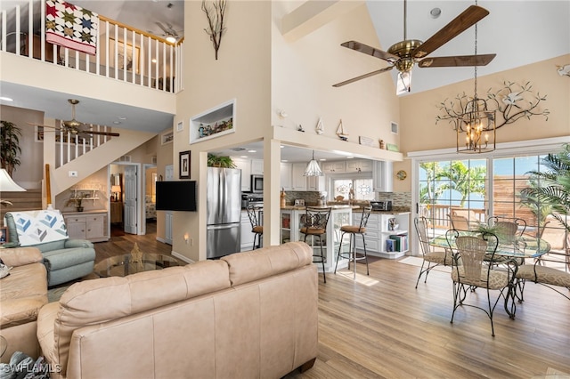 living area with a towering ceiling, ceiling fan with notable chandelier, and light wood-type flooring