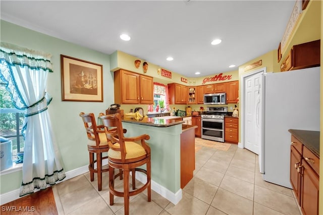 18511 Slater Rd, North Fort Myers, FL 33917 - kitchen featuring appliances with stainless steel finishes, a peninsula, a breakfast bar area, light tile patterned flooring, and dark countertops