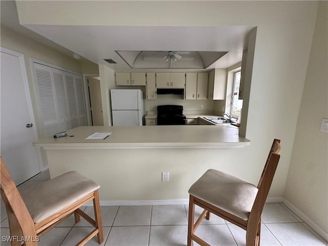 kitchen with light countertops, freestanding refrigerator, under cabinet range hood, visible vents, and black range with electric stovetop