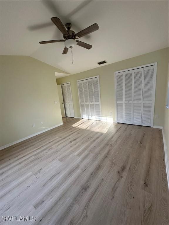 unfurnished bedroom with two closets, baseboards, vaulted ceiling, and wood finished floors