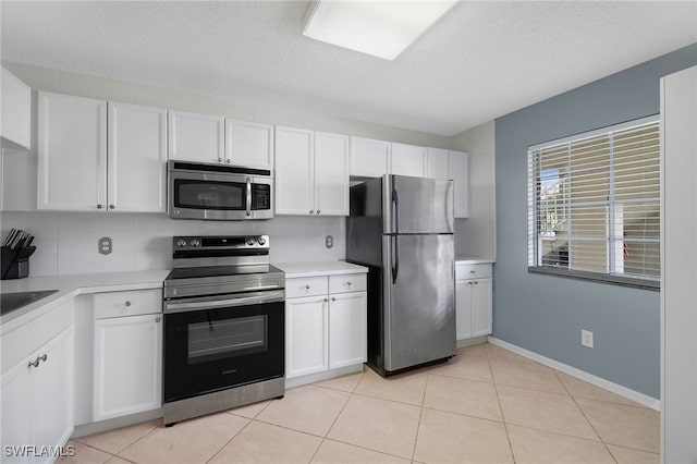 kitchen with appliances with stainless steel finishes, light countertops, white cabinets, light tile patterned floors, and a textured ceiling